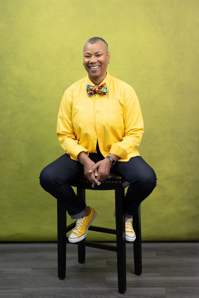 Karen Anastasia Prescod seated and smiling in a yellow shirt and colorful bow tie